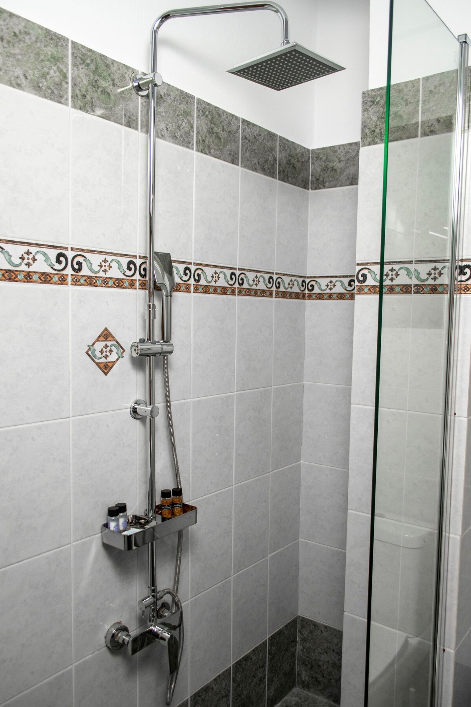 Ducha con mampara de vidrio, cabezal de ducha de mano y grifo de mano.