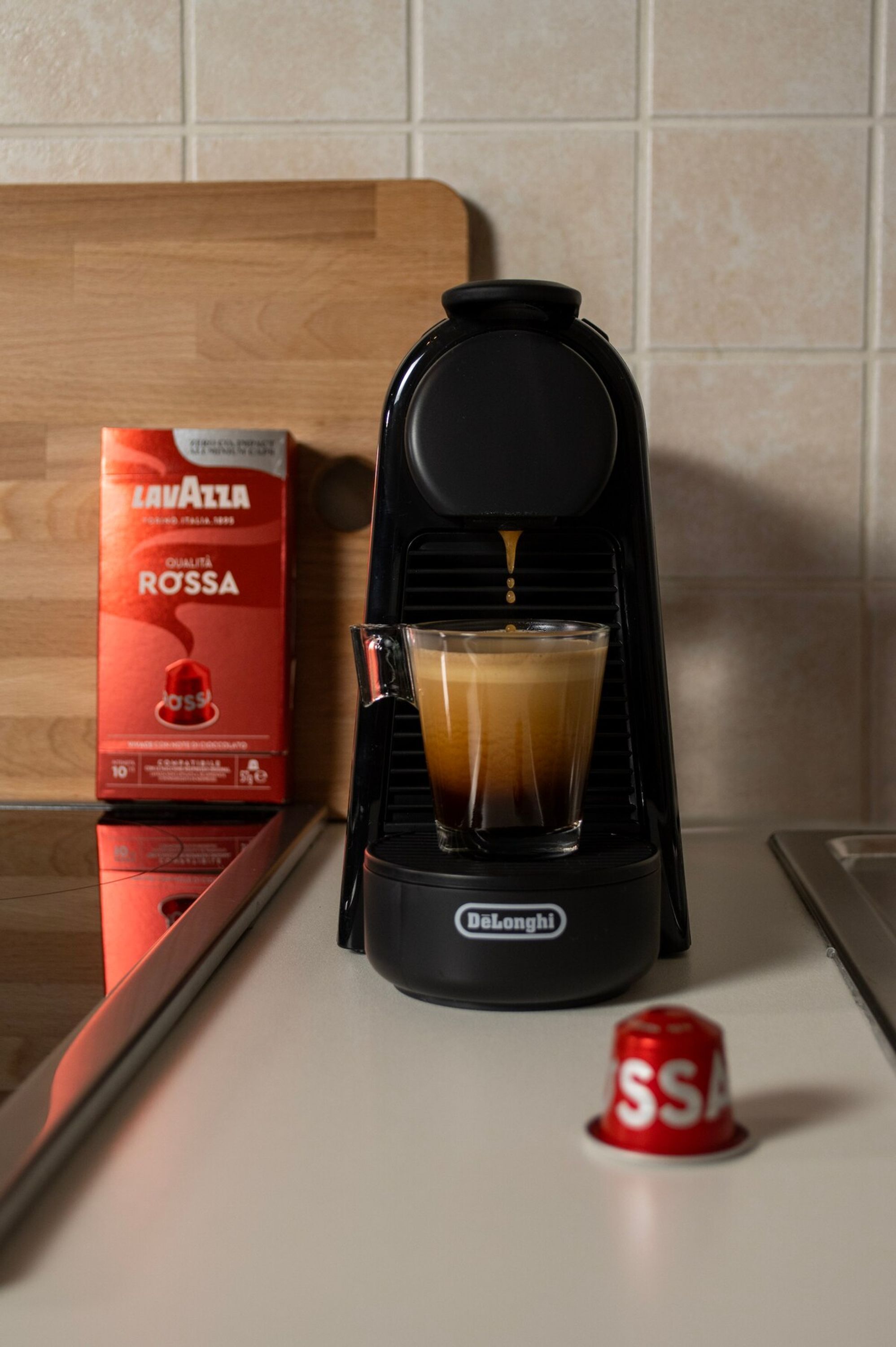 Una macchina del caffè con una tazza di caffè su un bancone della cucina, una confezione di caffè Lavazza e una cialda di caffè rossa.