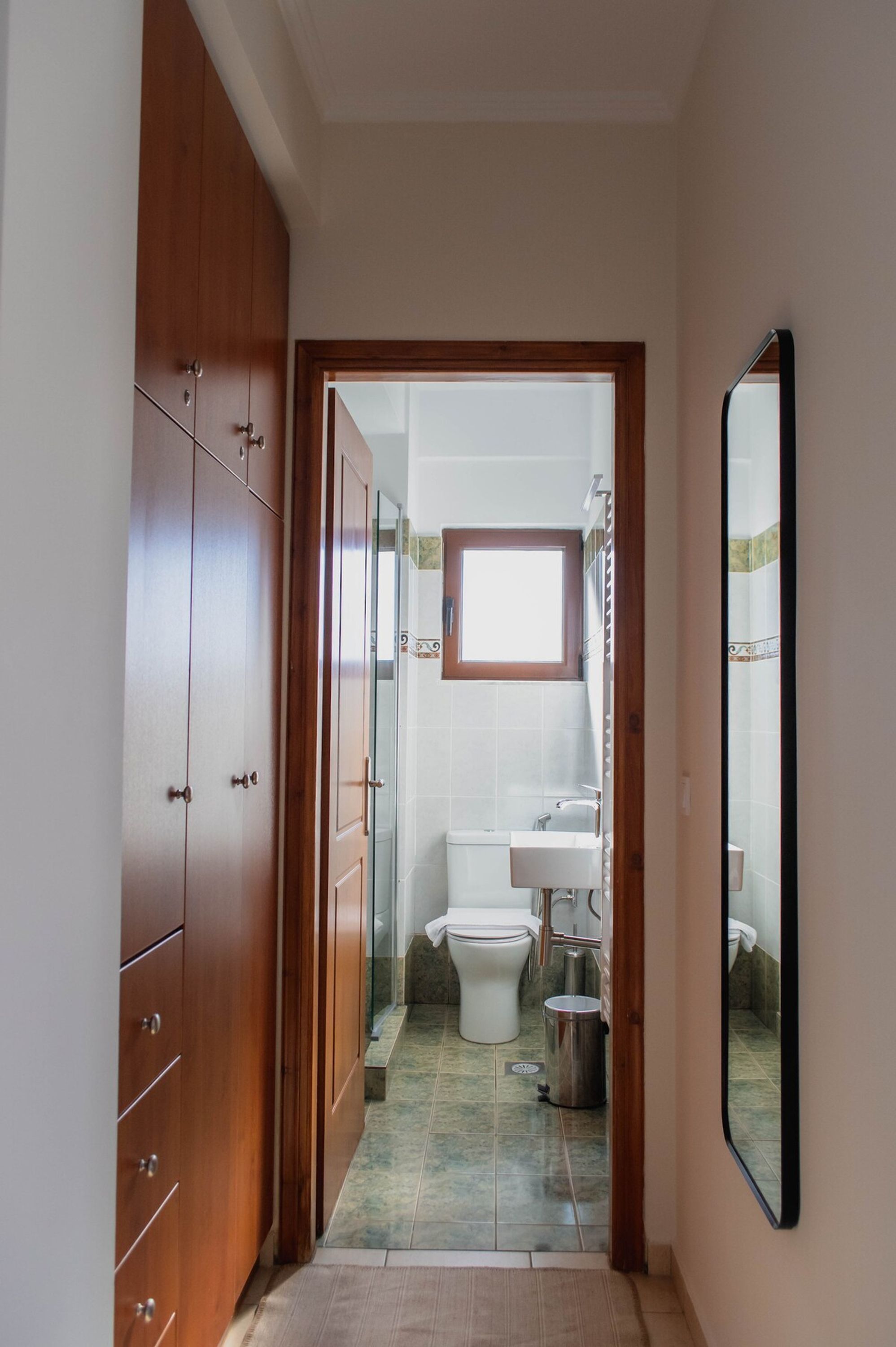 Ein schmaler Flur, der zu einem Badezimmer mit Toilette, Waschbecken und Duschbereich führt.