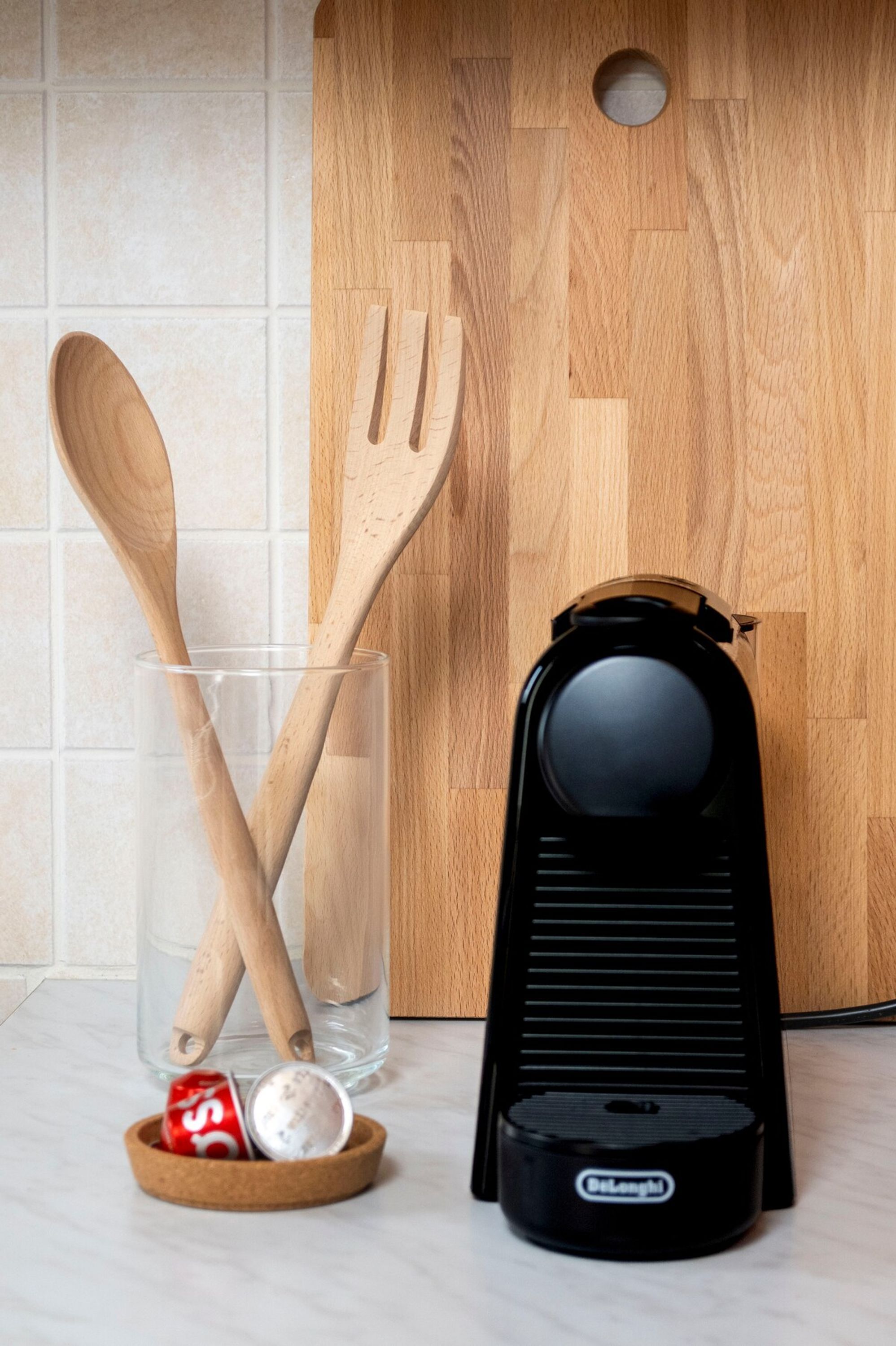 Una encimera de cocina con utensilios de madera, un vaso, una cafetera y un recipiente.
