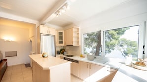 A modern kitchen with light wood cabinets, a central island, a built-in oven, and a large window providing a view of trees.