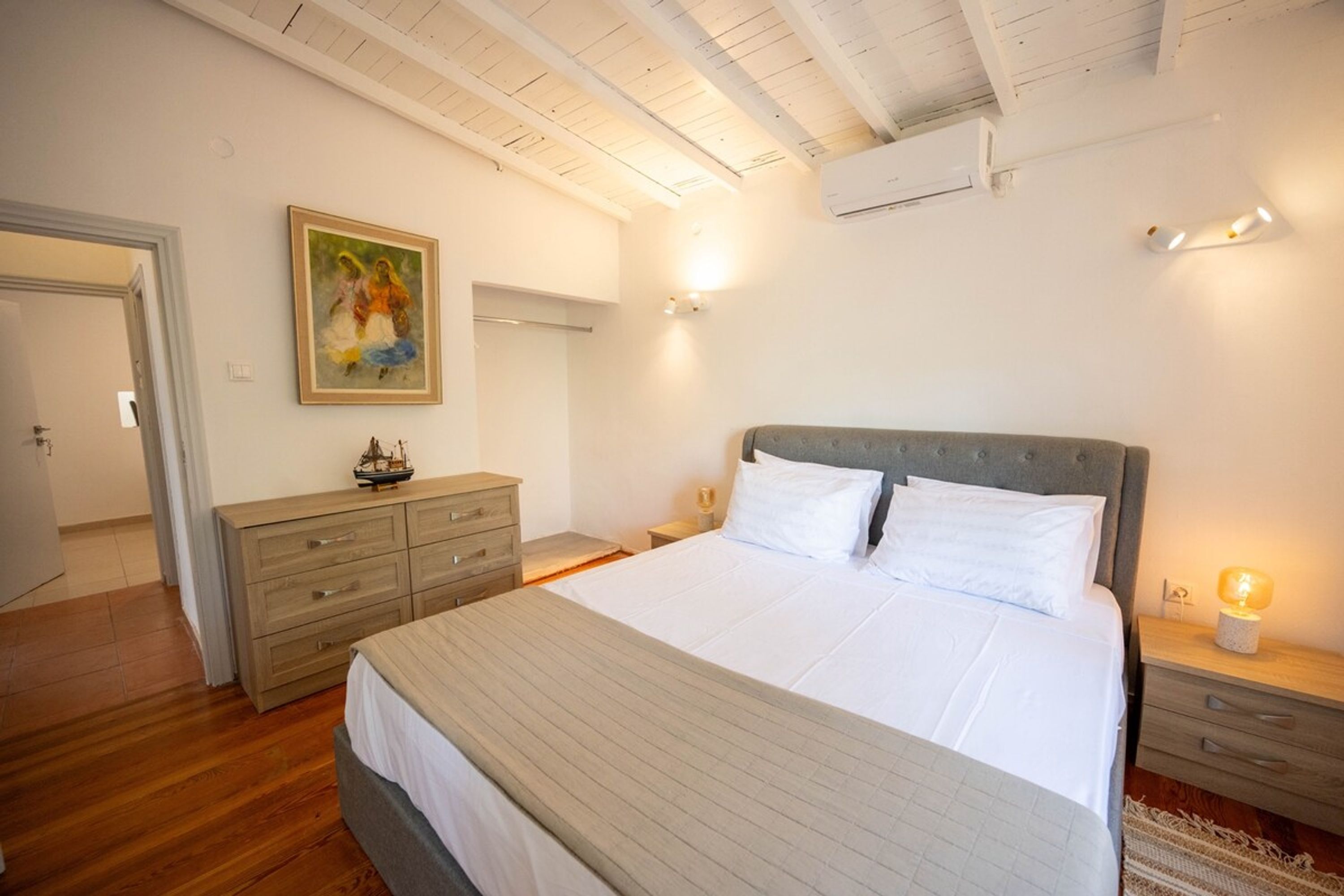 Una camera da letto con un letto grande, una cassettiera, un comodino, un condizionatore d'aria a parete e un quadro appeso al muro.