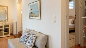 A bedroom with a bed, a bedside table, a lamp, a framed picture on the wall, and a door leading to another room.