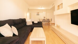 Un salon moderne avec un canapé de couleur sombre, une table basse en bois et un téléviseur à écran plat fixé au mur.