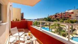 Un balcon avec une table préparée pour le petit-déjeuner, donnant sur une piscine et un quartier résidentiel.