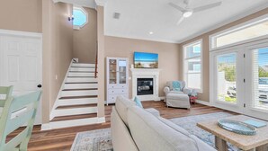 A spacious living room with a staircase, a fireplace, and a large window with blinds.