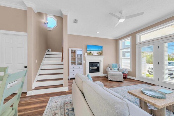 A spacious living room with a staircase, a fireplace, and a large window with blinds.