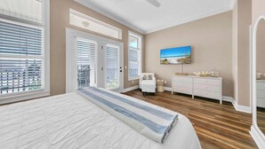 A bedroom with a large bed, a ceiling fan, a painting, a dresser, and a window with blinds.