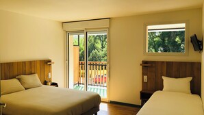 Habitación de hotel con dos camas, suelo de madera, balcón con vista a árboles y ventana con vista al exterior.