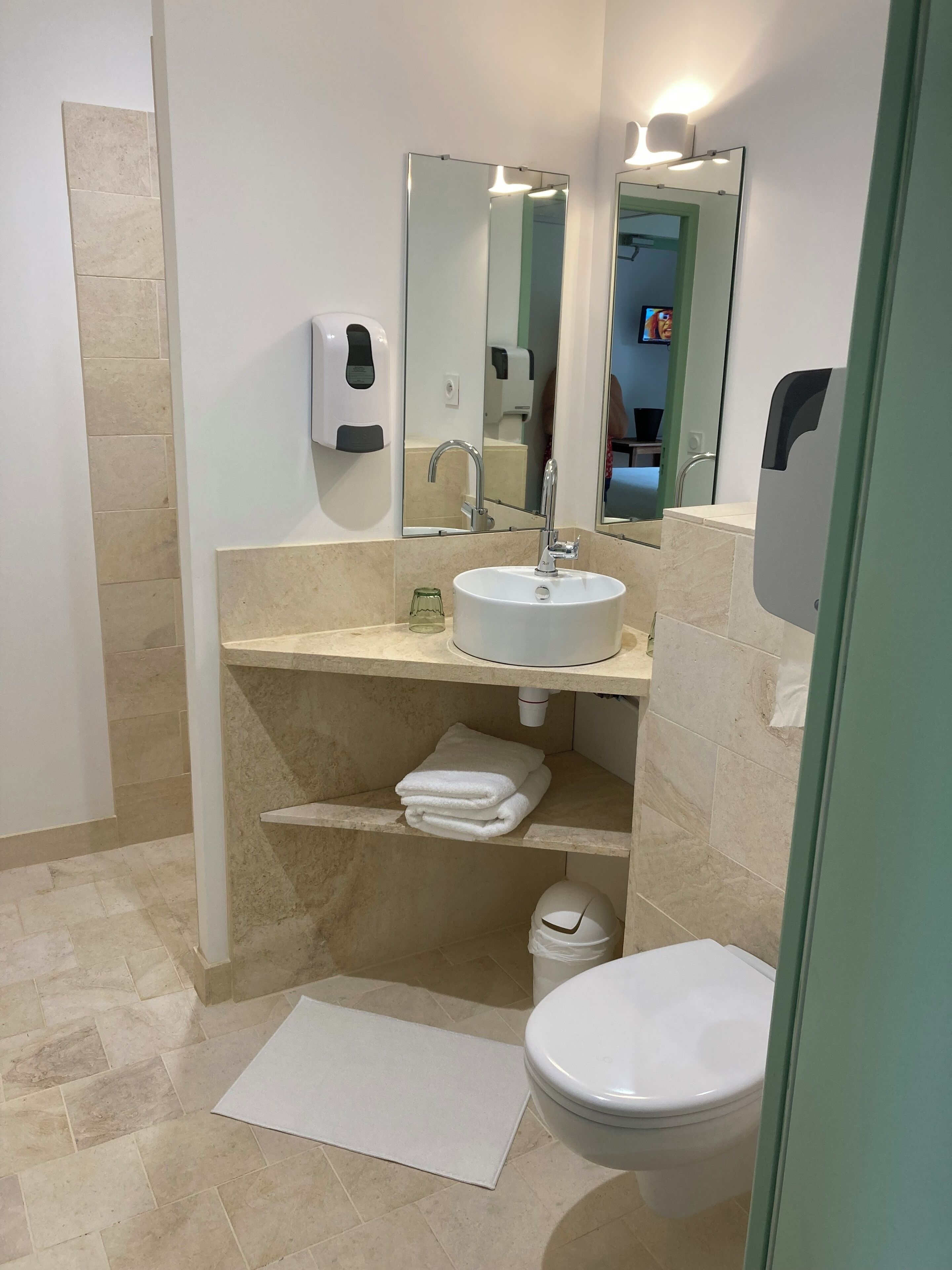 Un baño moderno con un lavamanos blanco, un espejo, un inodoro y una repisa con toallas dobladas.