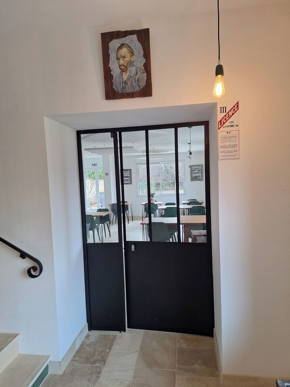 A room with a black door, a framed portrait above it, and a light bulb hanging from the ceiling.