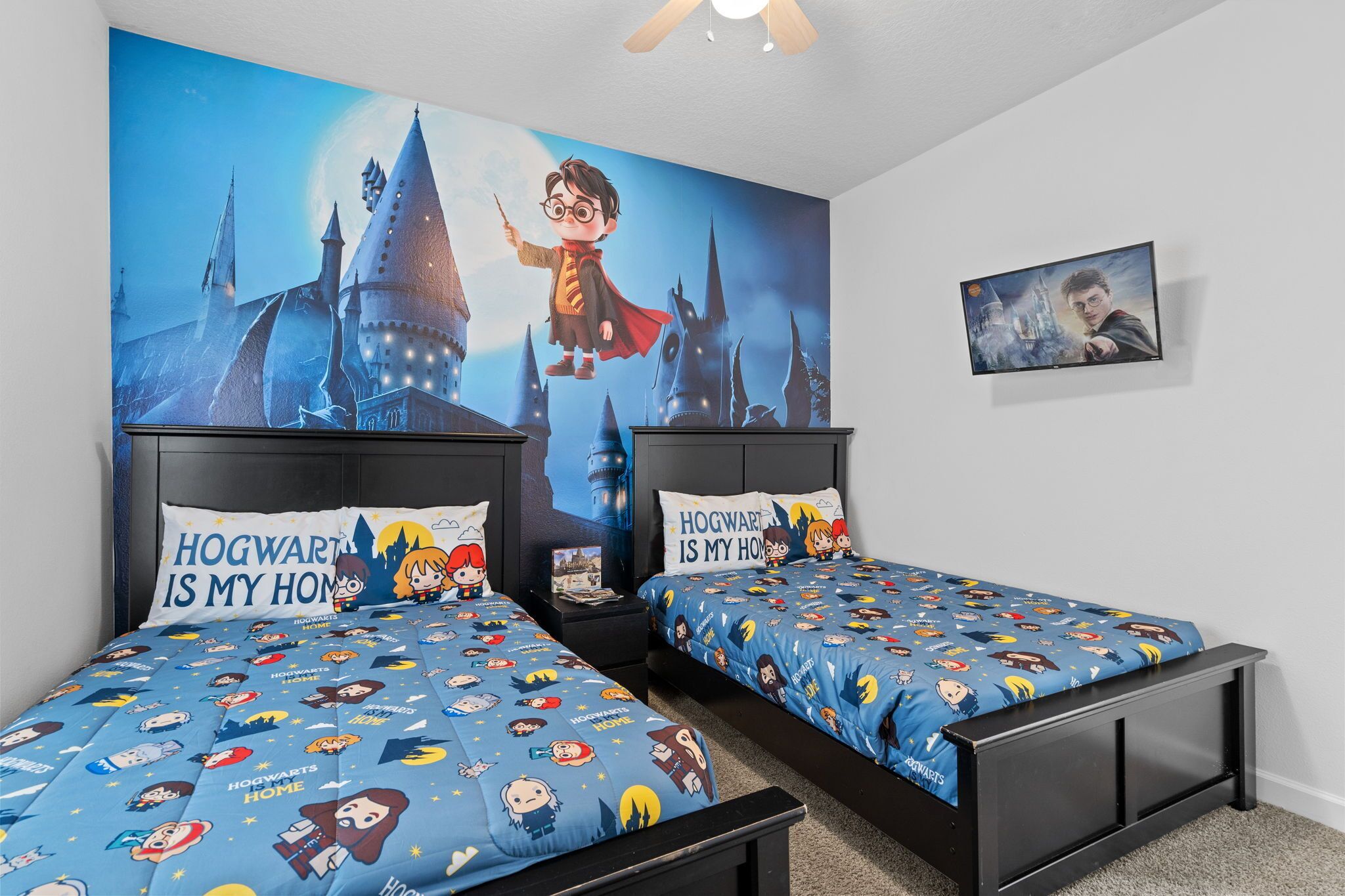 Une chambre avec deux lits, chacun recouvert d'une couette et agrémenté d'oreillers aux couleurs et motifs de Poudlard.