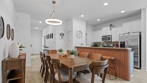 A modern kitchen with white cabinets, stainless steel appliances, and a wooden dining table with chairs. - Modern 5BR Retreat w/ Pool and Clubhouse Access (Kissimmee)