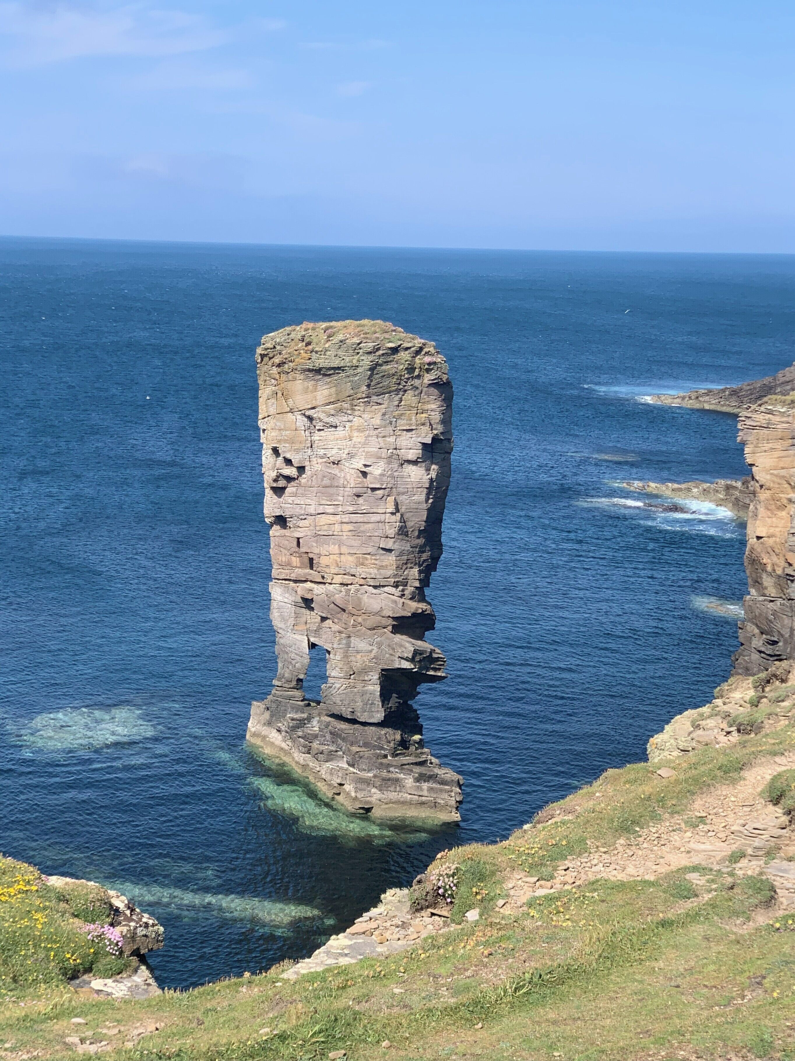 A coastal cliff with a prominent rock formation extending into the sea.
