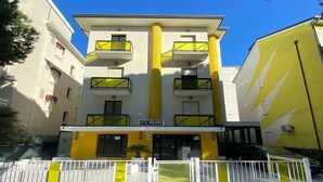 A hotel with a yellow facade, multiple balconies, and a sign indicating it is a hotel. - Hotel Bologna (Rimini)
