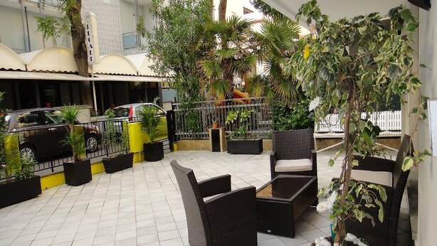 An outdoor patio area with tiled flooring, black wicker furniture, and potted plants. - Hotel Bologna (Rimini)