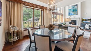 A modern dining area with a round glass table, white upholstered chairs, and a decorative centerpiece. - Rare Two Story Condo in Ritz-Carlton by InvitedHome | Pool, Hot Tub, Lounge, Gym (Vail)