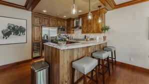 A kitchen with wooden cabinets, a marble island, bar stools, pendant lights, and a stainless steel refrigerator. - Rare Two Story Condo in Ritz-Carlton by InvitedHome | Pool, Hot Tub, Lounge, Gym (Vail)