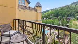 A balcony with a chair and table, overlooking a pool and a forested area. - Rare Two Story Condo in Ritz-Carlton by InvitedHome | Pool, Hot Tub, Lounge, Gym (Vail)