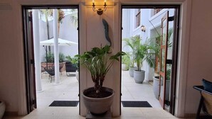 Entrada de hotel con una planta en maceta en el centro, una puerta con felpudo y vistas al patio exterior.