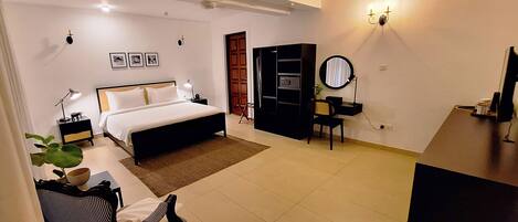 A hotel room with a bed, bedside tables, a desk, a chair, a wardrobe, a mirror, and a TV.