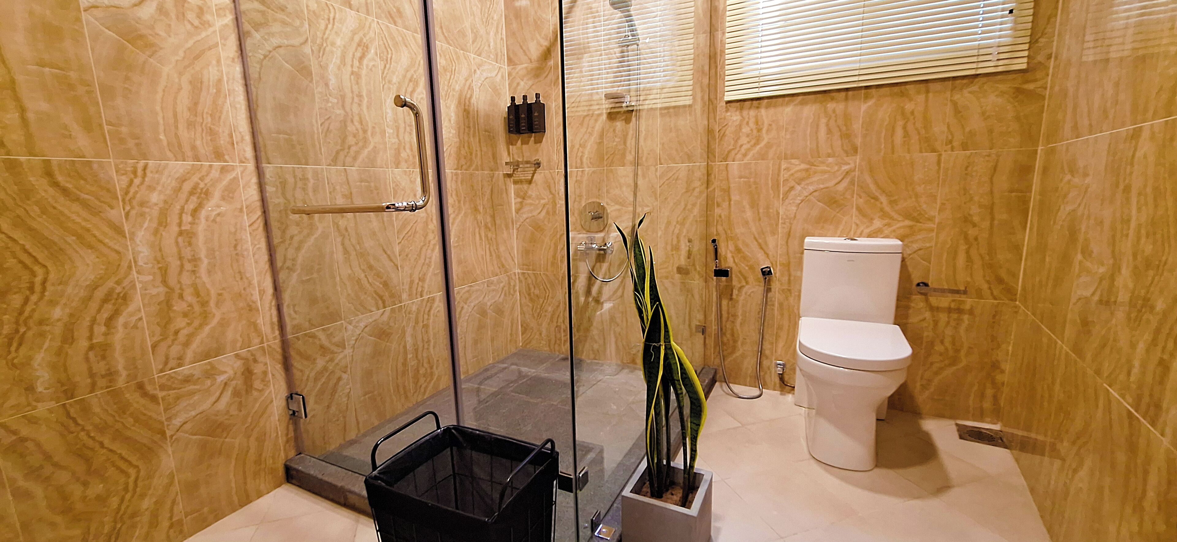 Un baño con ducha envuelta en vidrio, un inodoro y un cubo de basura negro.