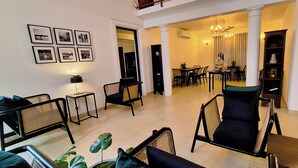 Una sala de estar moderna con comedor, con muebles negros y de mimbre, una araña y una escalera que sube a un nivel superior.