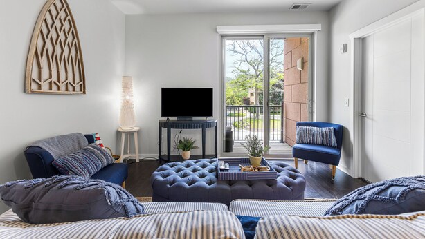 A modern living room with a large TV, comfortable seating, and a view through a sliding glass door. - Cozy Nautical Themed 2-bedroom condo with AC in charming Traverse City. (Traverse City)