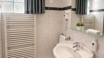 A bathroom with a white sink, a glass shelf with toiletries, a towel rack, a mirror, and a window with curtains.