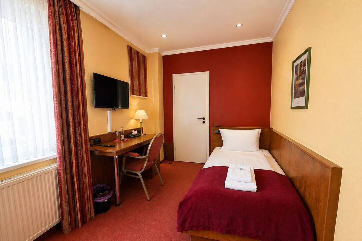 A hotel room with a bed, a desk, a chair, a television, and a door.