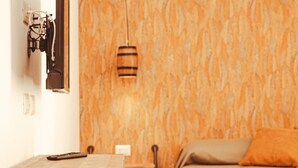 A room with a wooden barrel stool, a bed with an orange pillow, and a table with a remote control. - U Zuccareddu (Alcamo)
