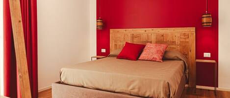 A bed with a wooden headboard, red pillows, and a brown bedspread in a room with red walls and wooden flooring.