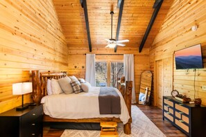 Un dormitorio de cabaña de madera con cama, mesita de noche, lámpara y televisor en la pared.