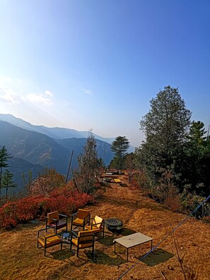 Un espace aménagé avec des chaises et une table, entouré d’arbres et offrant une vue sur les montagnes lointaines.