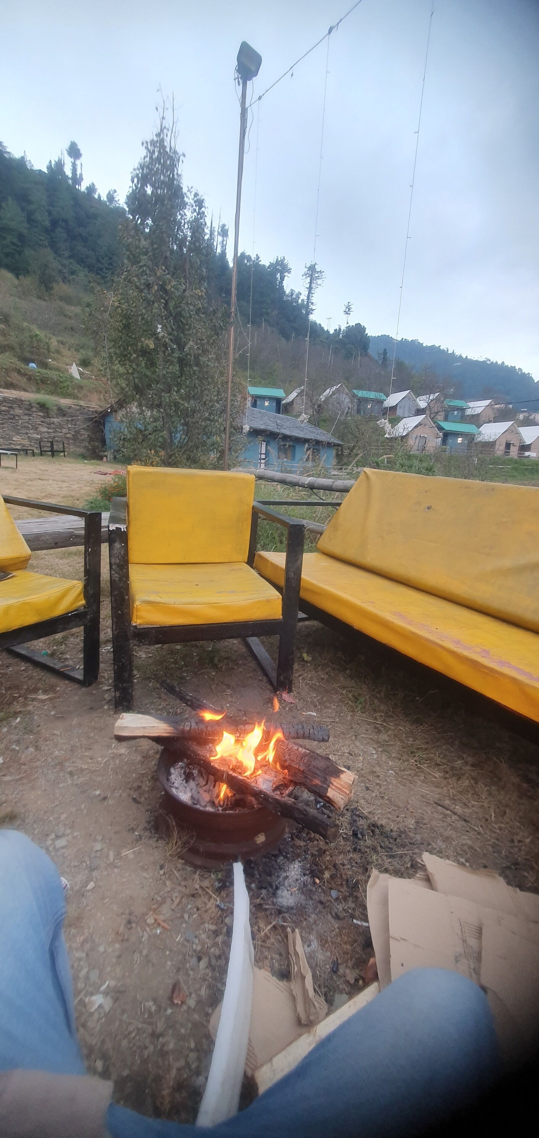 A rustic outdoor seating area with yellow chairs and a campfire.