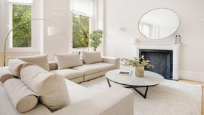 A modern living room with a beige sofa, a round coffee table, a fireplace, and a large mirror on the wall. - Elegant 3-Bedroom Luxury Retreat in Prestigious Cadogan Square (London)