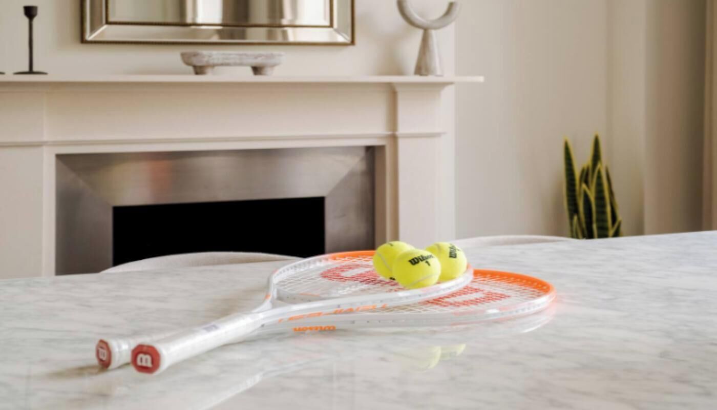 A tennis racket and two tennis balls on a marble surface.