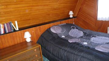 A bedroom with a wooden bunk bed, a bedside table with a lamp, and a shelf with books.