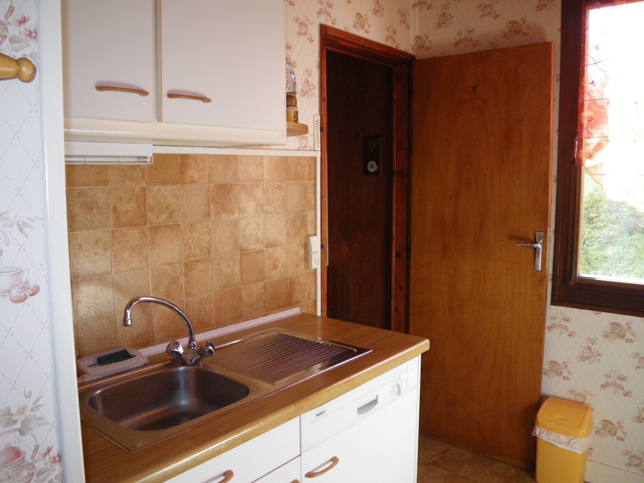 Een kleine keuken met een spoelbak, een houten aanrechtblad en een deur naar een andere kamer.