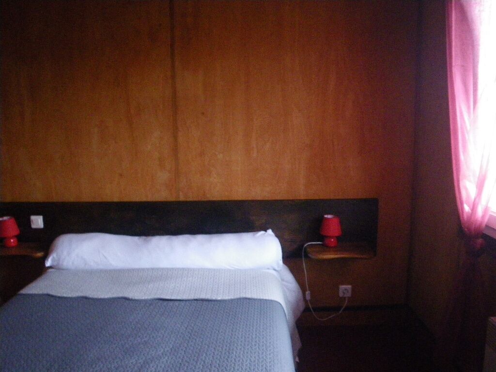 Un lit avec une tête de lit en bois, deux tables de chevet avec des lampes rouges et une prise électrique sur le mur.