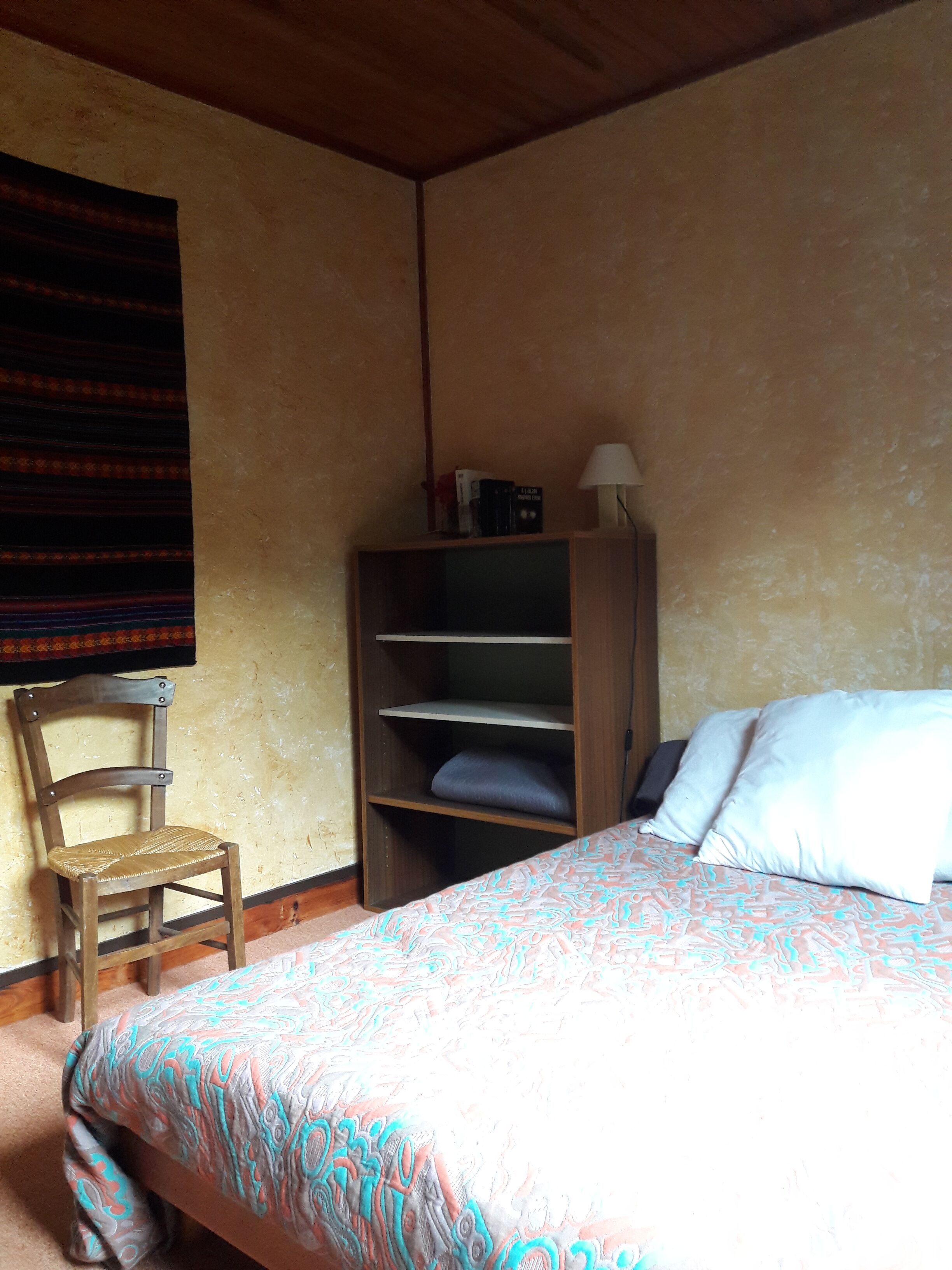 Un dormitorio con cama, una silla de madera, una estantería y una lámpara.