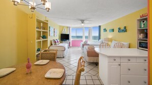 A bright room with a dining table, two beds, a ceiling fan, and a view of the ocean. - Top of the Gulf by Book That Condo (Panama City Beach)