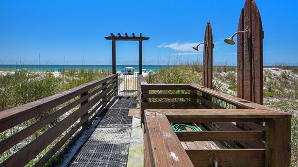 A wooden boardwalk leading to a beach with a pergola and a beach umbrella. - Top of the Gulf by Book That Condo (Panama City Beach)