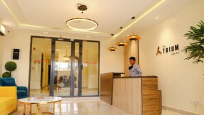 A modern reception area with a wooden reception desk, a glass door entrance, a round gold table, and a potted plant. - THE ATRIUM LAGOS (Lagos)