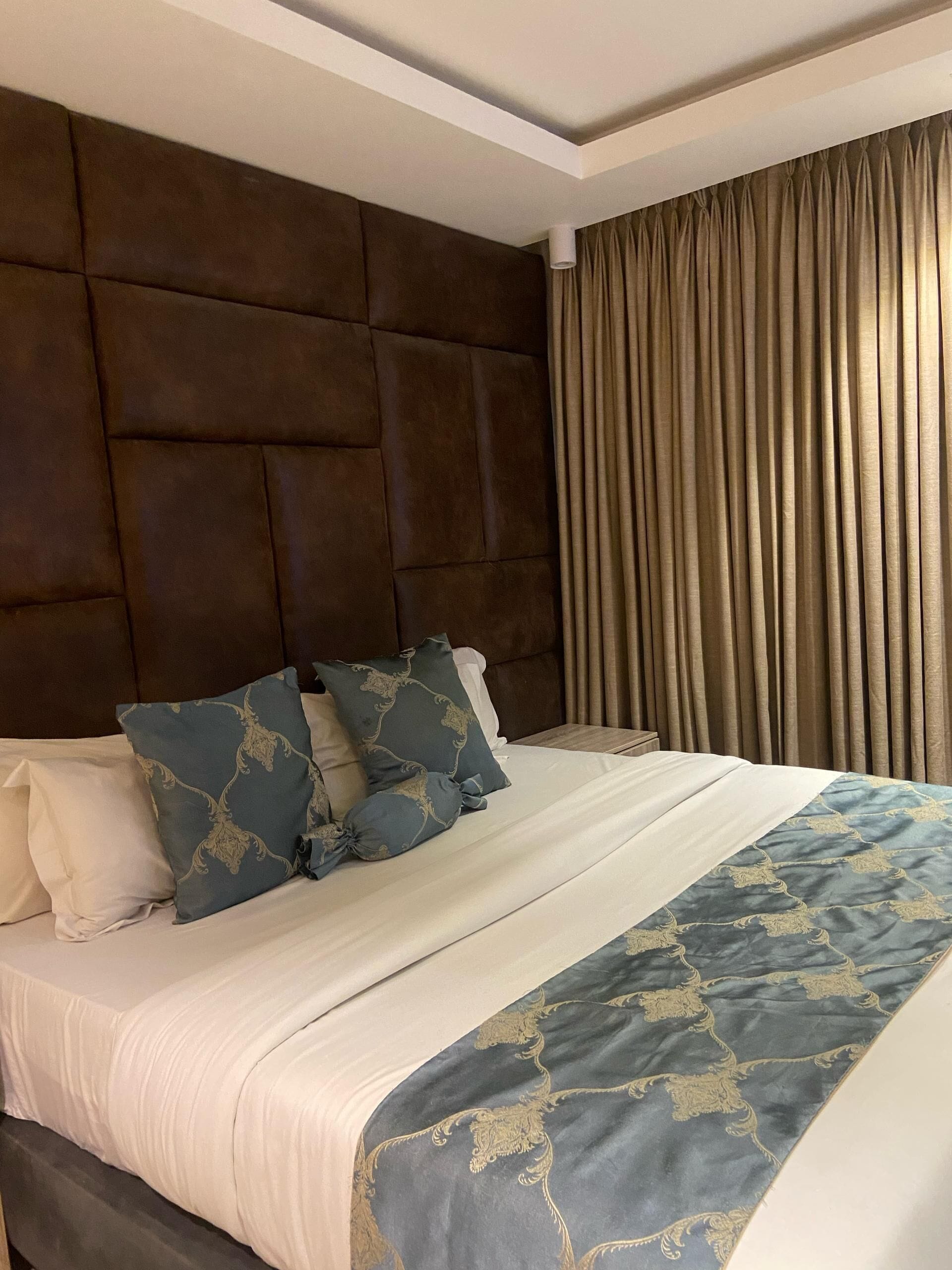 A hotel room with a large bed, a headboard, and a window with curtains.