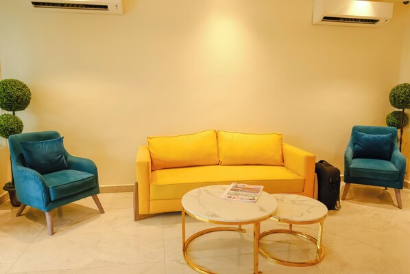 A room with a yellow sofa, two teal armchairs, a marble coffee table, and a black suitcase. - THE ATRIUM LAGOS (Lagos)