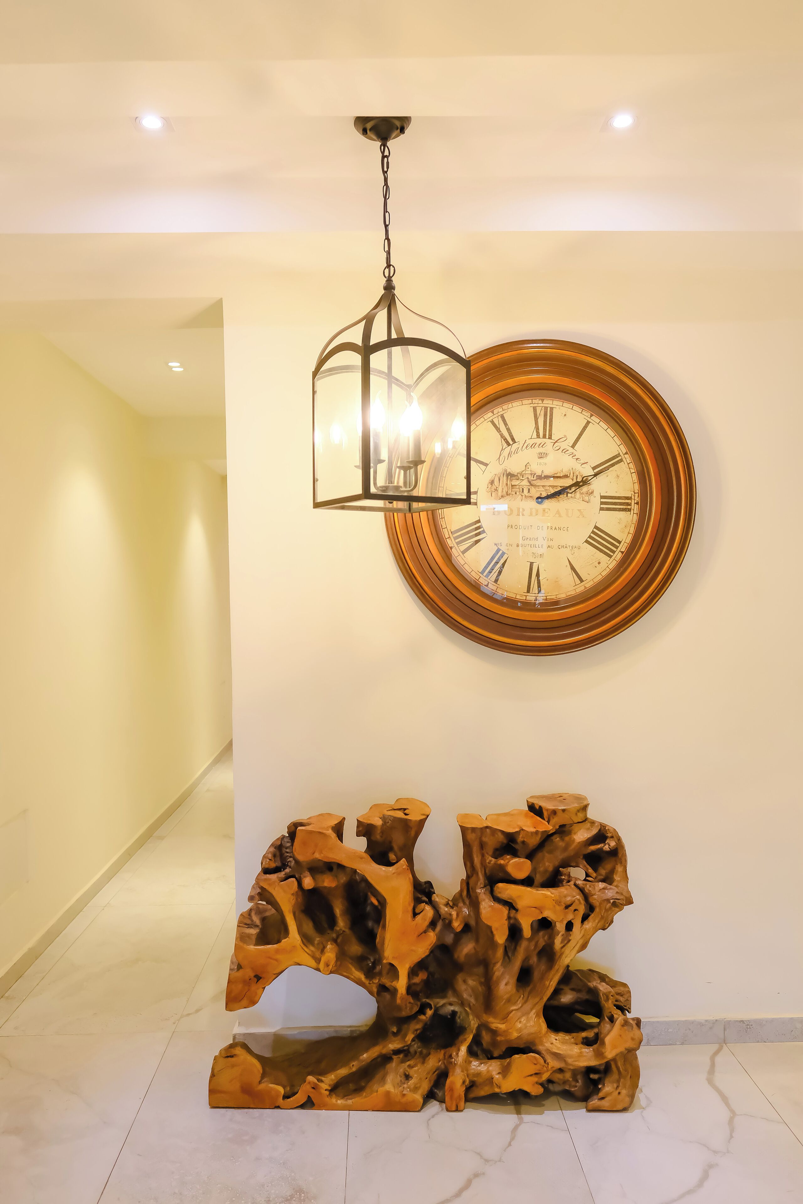 A wall-mounted clock with Roman numerals and a wooden sculpture.