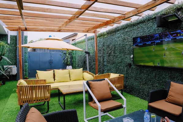 A patio area with outdoor furniture, a TV screen, and a green hedge wall. - THE ATRIUM LAGOS (Lagos)