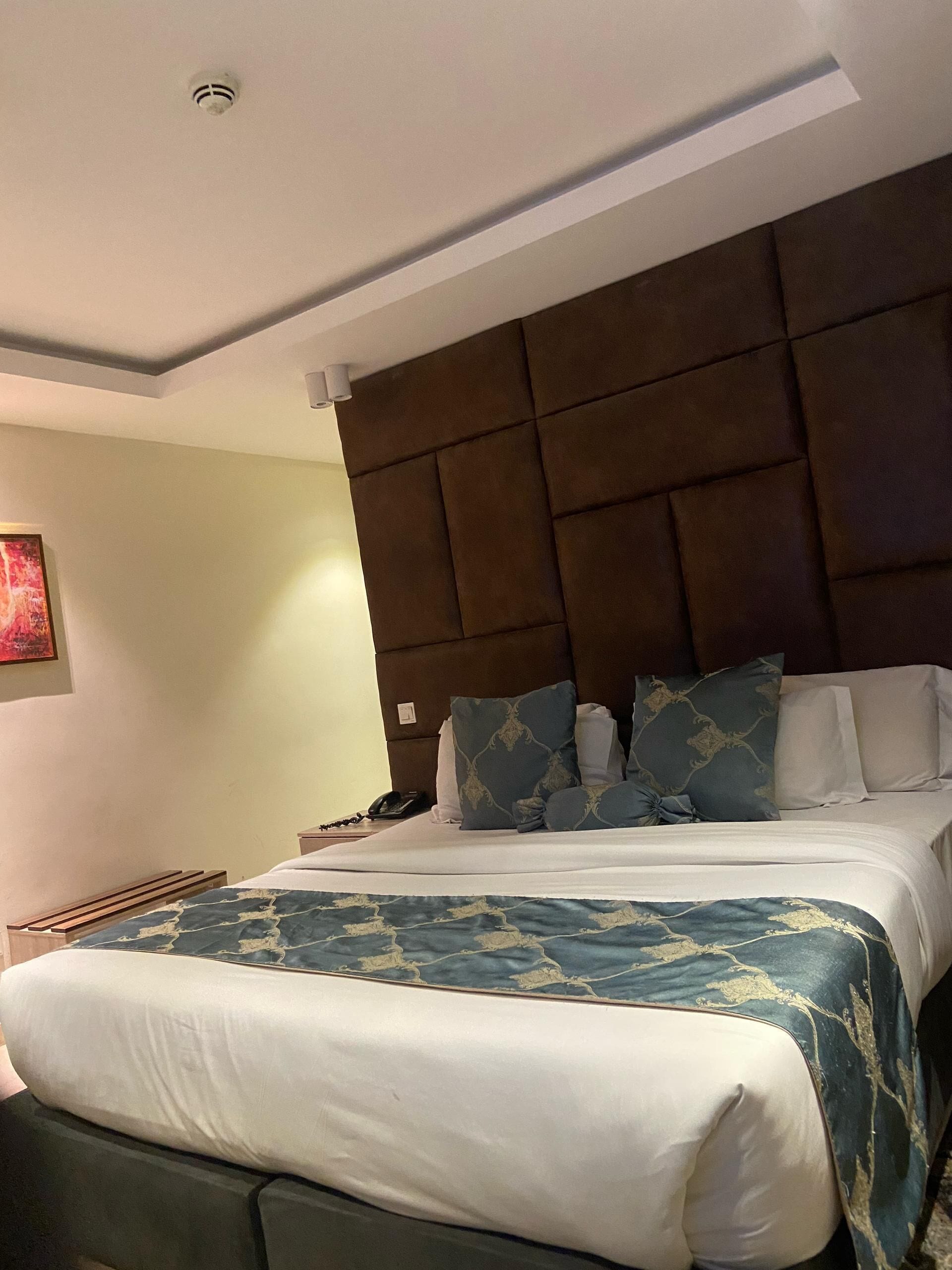 Ein Hotelzimmer mit einem großen Bett, einem Kopfteil und einem Nachttisch mit Telefon.