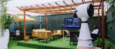 A patio area with artificial grass, wooden furniture, and a large fan.